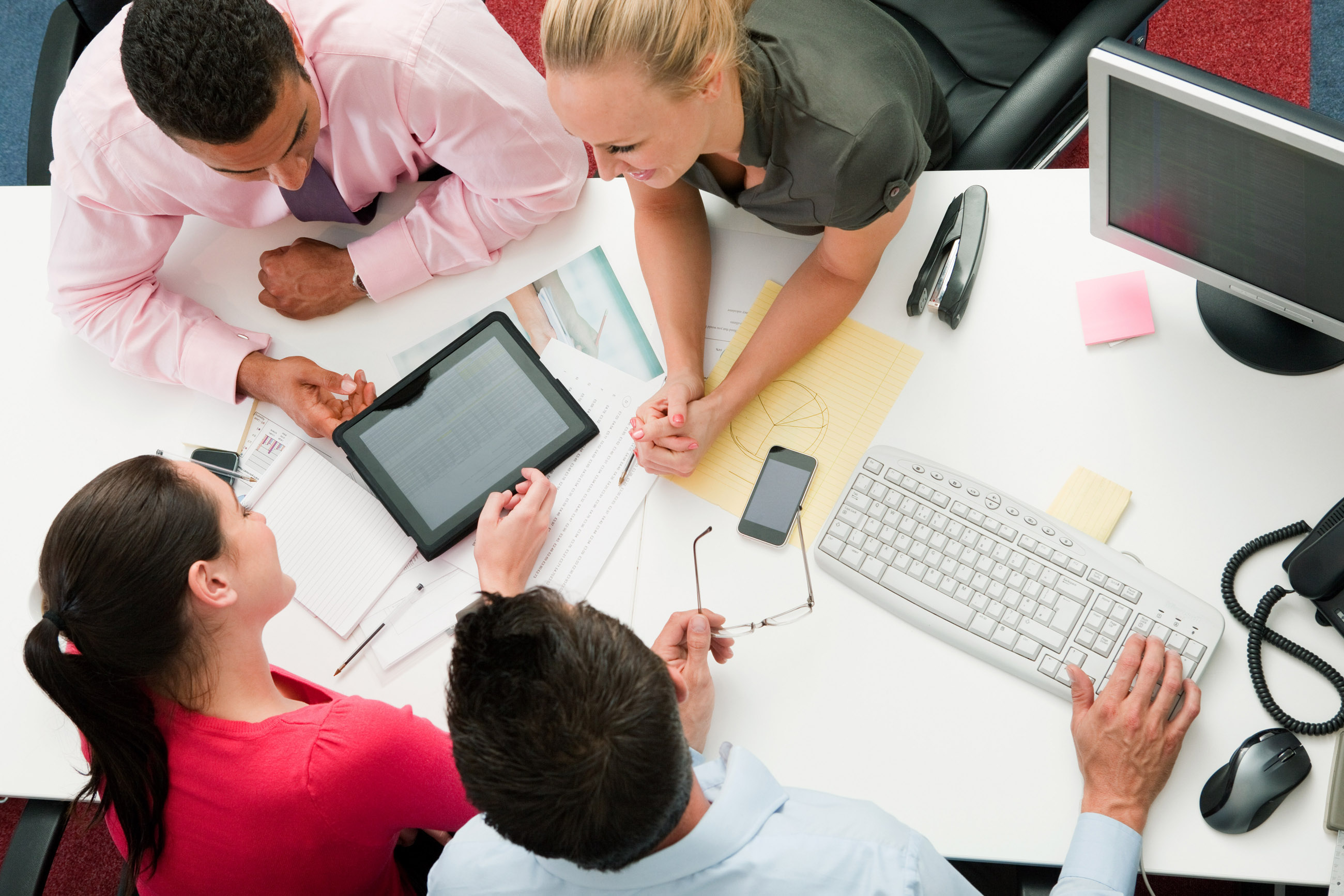 Four employees gathered around a digital tablet --- Image by © Neil Guegan/Image Source/Corbis